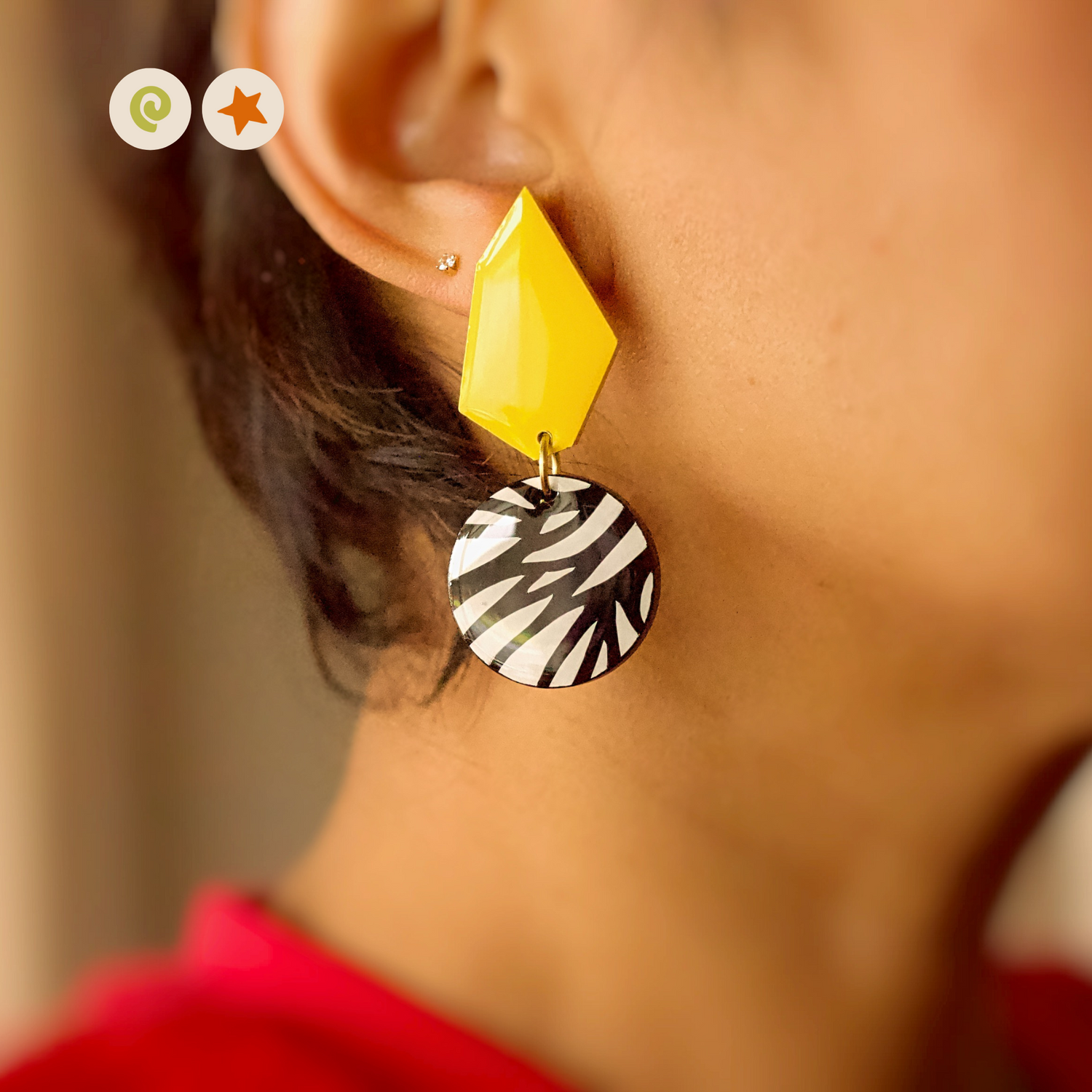 Earrings with a yellow geometric shape on top, and a black and white circle section at the bottom with a triangle pattern.