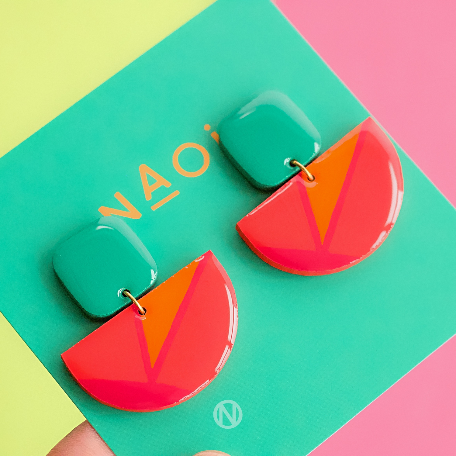 Earrings with a turquoise rounded rectangle shape on top, and a pink and orange semi circle section on the bottom.