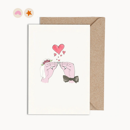 Card with an illustration of two hand kissing with hearts, one wearing a veil and one a bow tie.